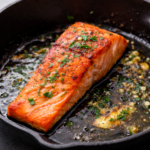 Pan seared salmon fillet cooked in a skillet with garlic butter