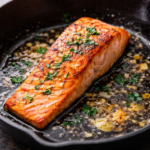 Pan seared salmon fillet cooked in a skillet with garlic butter sauce